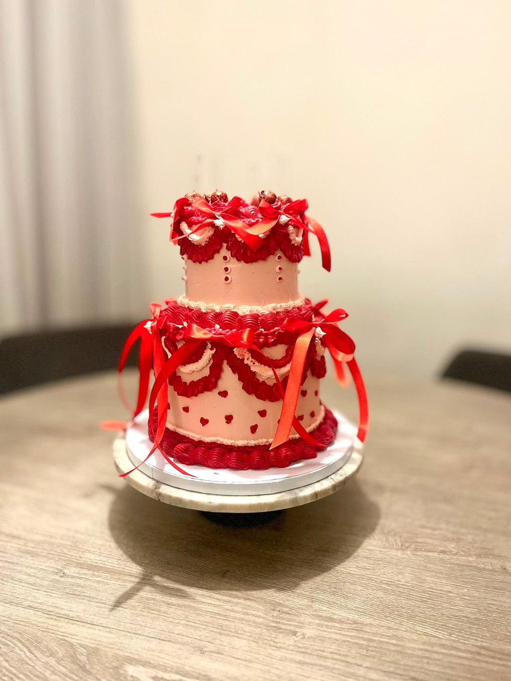Romantische tweelaagse vintage taart van Cake Magic met rode botercrème, elegante strikken, hartjes en handgespoten details. Luxe feesttaart voor een verjaardag, jubileum of bruiloft in Schiedam en omgeving Rotterdam.