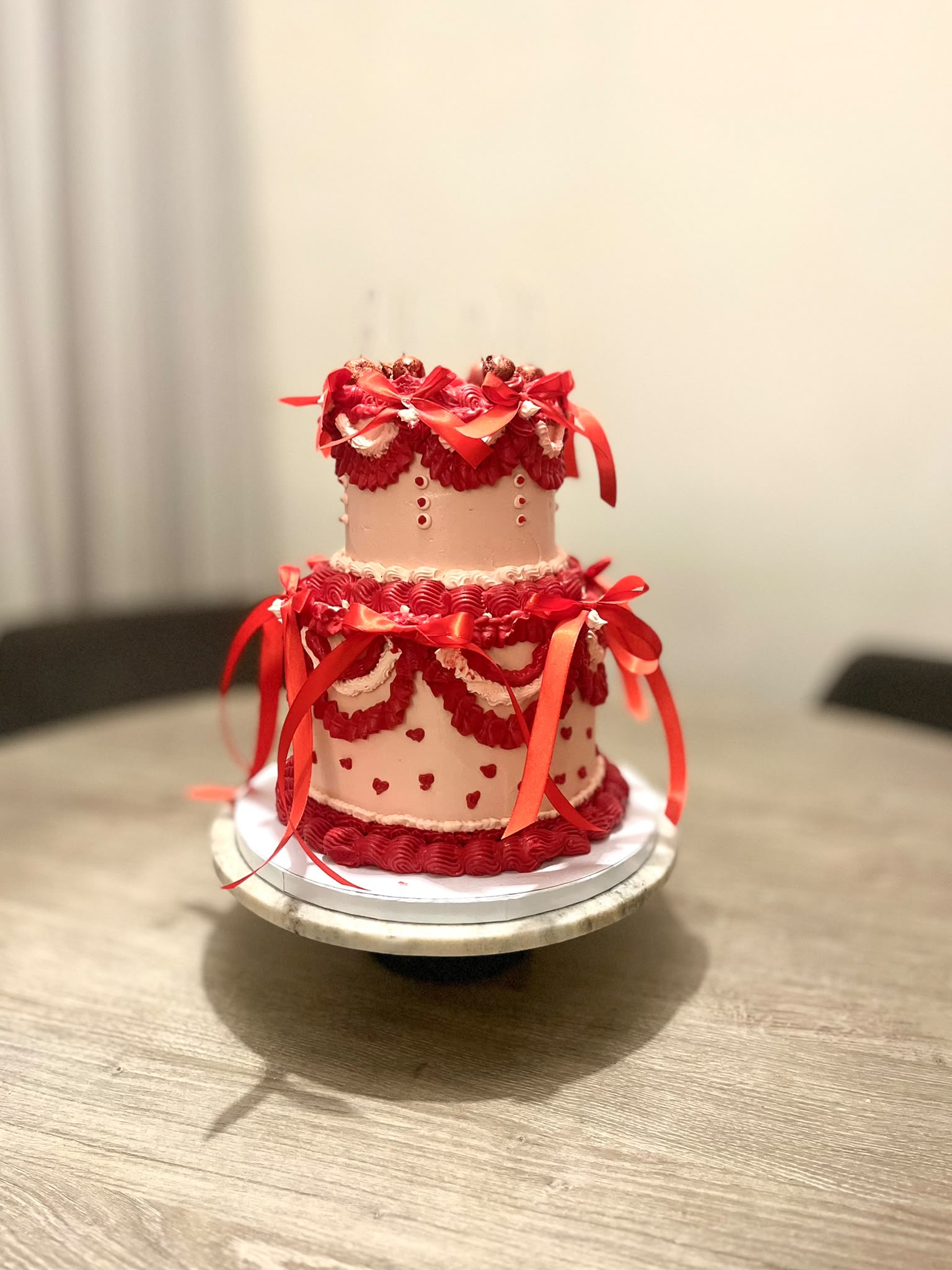 Romantische tweelaagse vintage taart van Cake Magic met rode botercrème, elegante strikken, hartjes en handgespoten details. Luxe feesttaart voor een verjaardag, jubileum of bruiloft in Schiedam en omgeving Rotterdam.